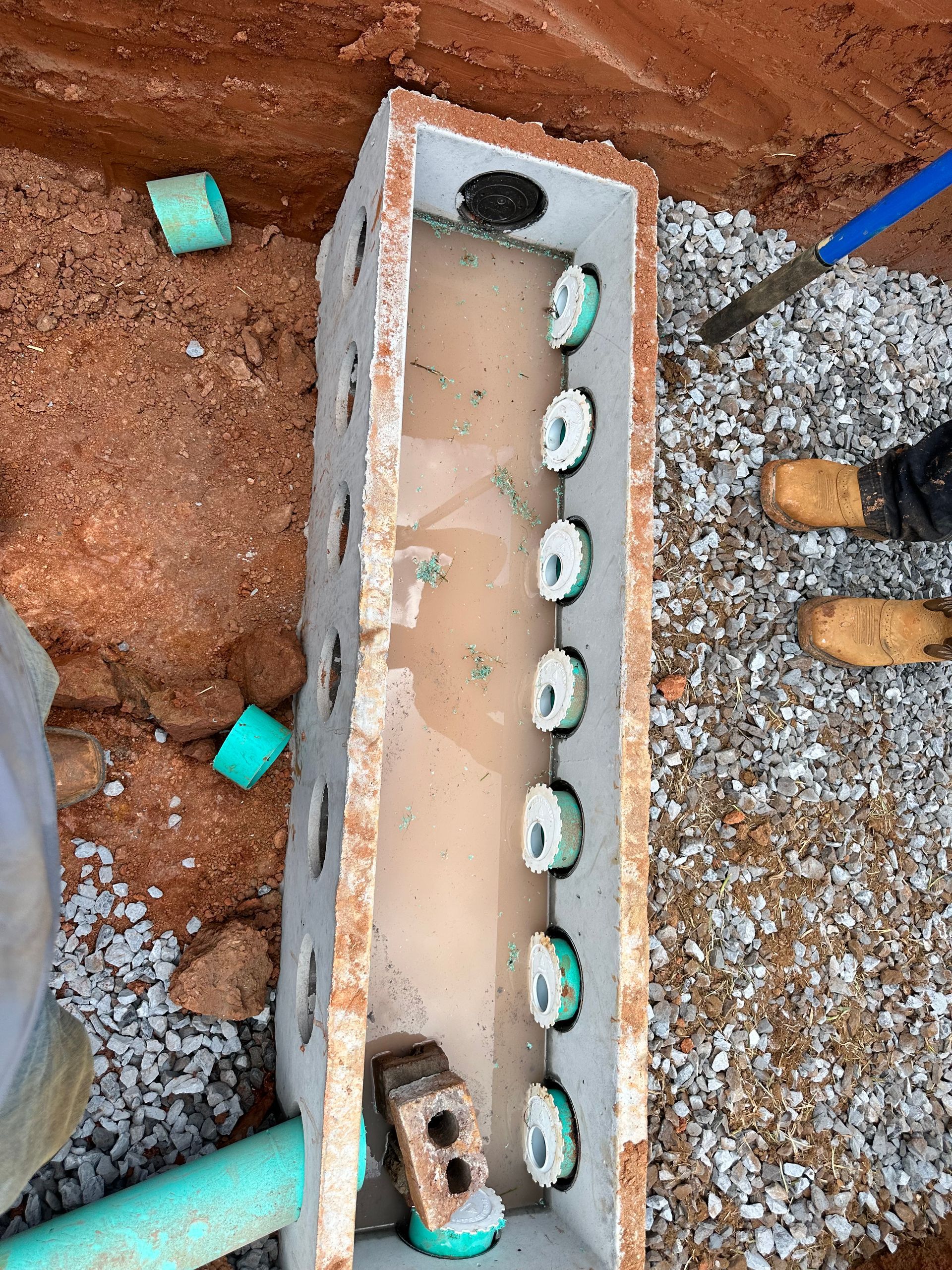 Open concrete trench with a row of white pipe fittings and construction debris around it