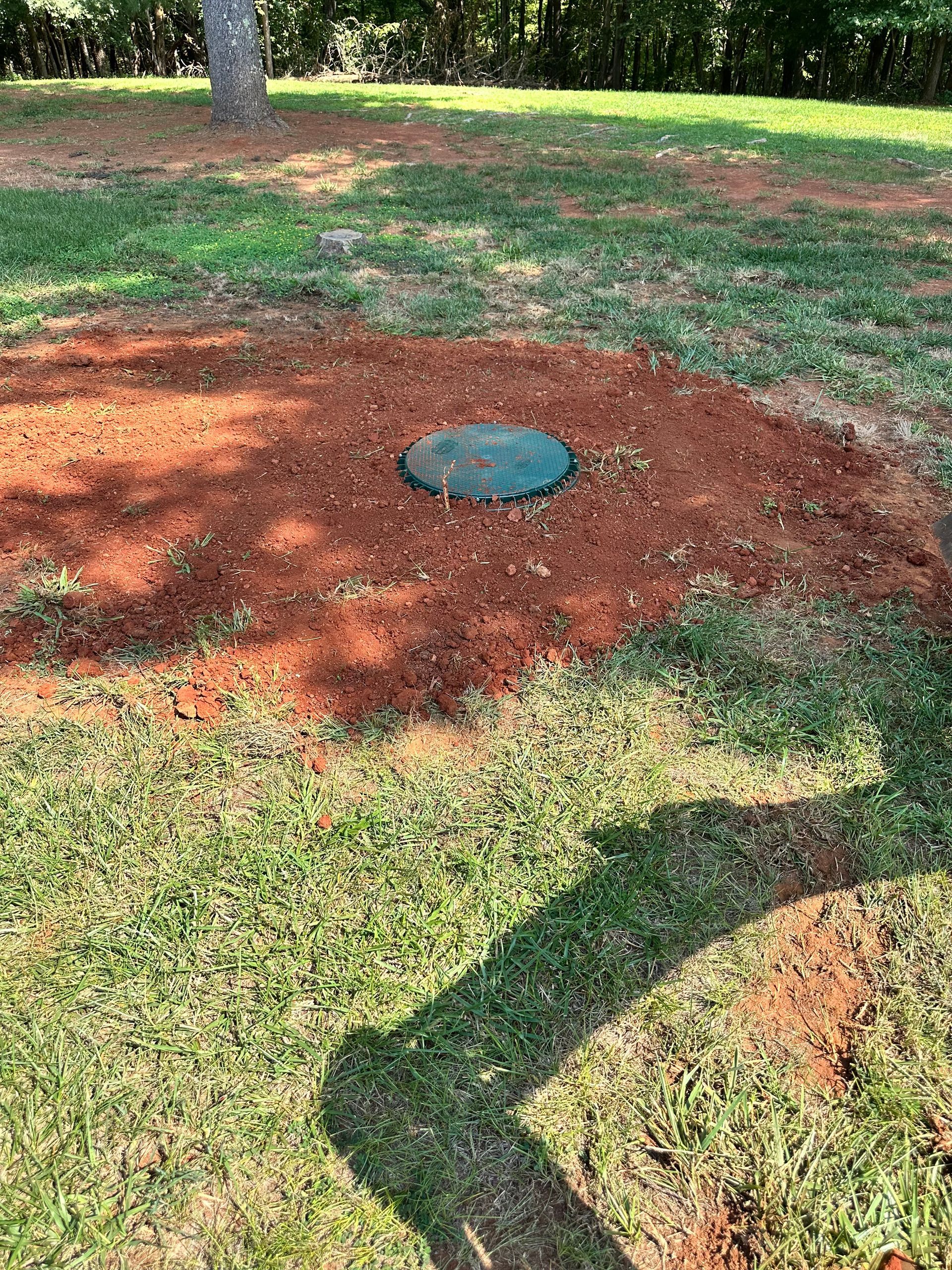 Circular utility cover in a red mulch patch on a grassy lawn.