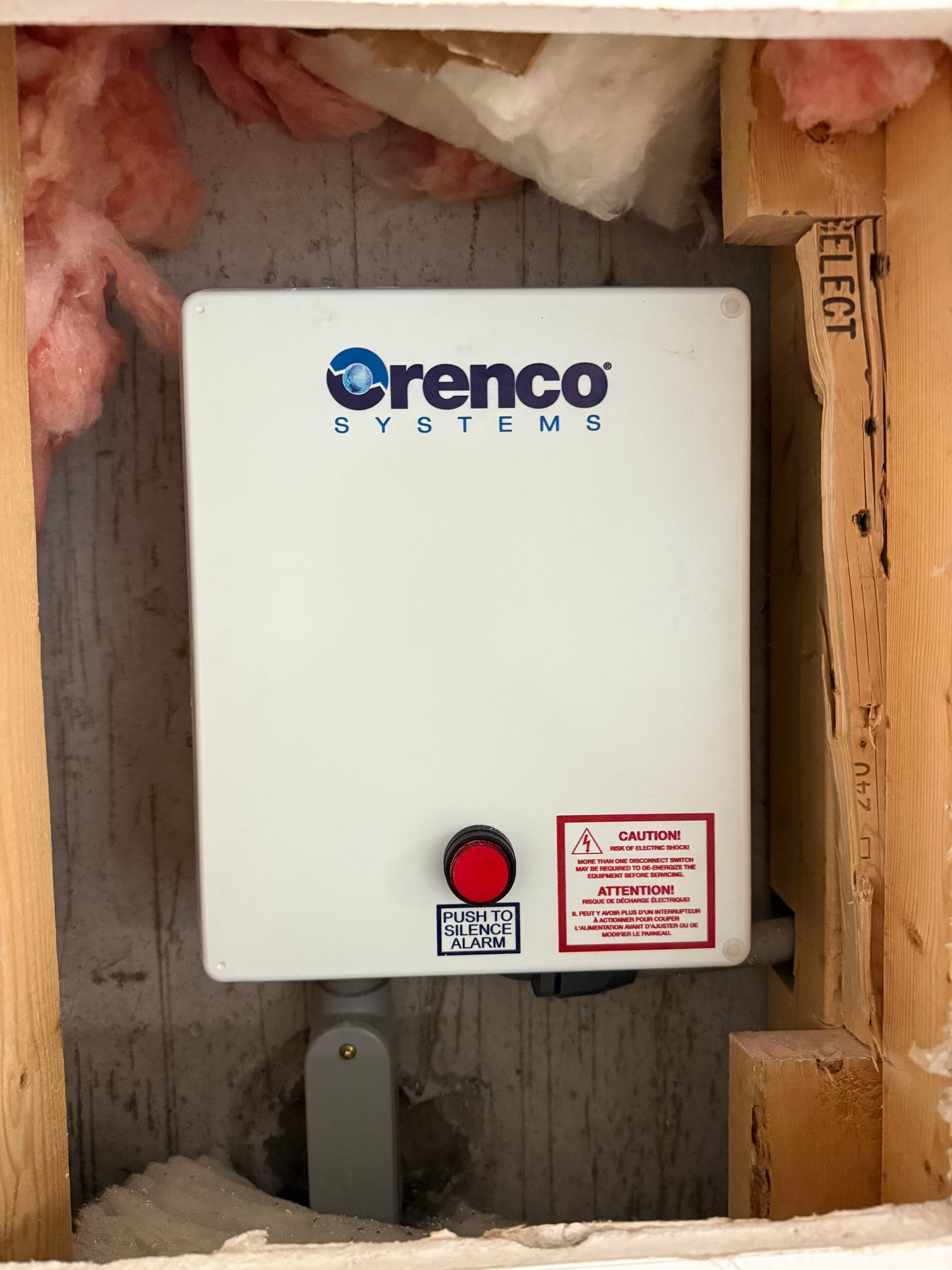 Orenco Systems control panel mounted in an unfinished wall with exposed insulation and framing