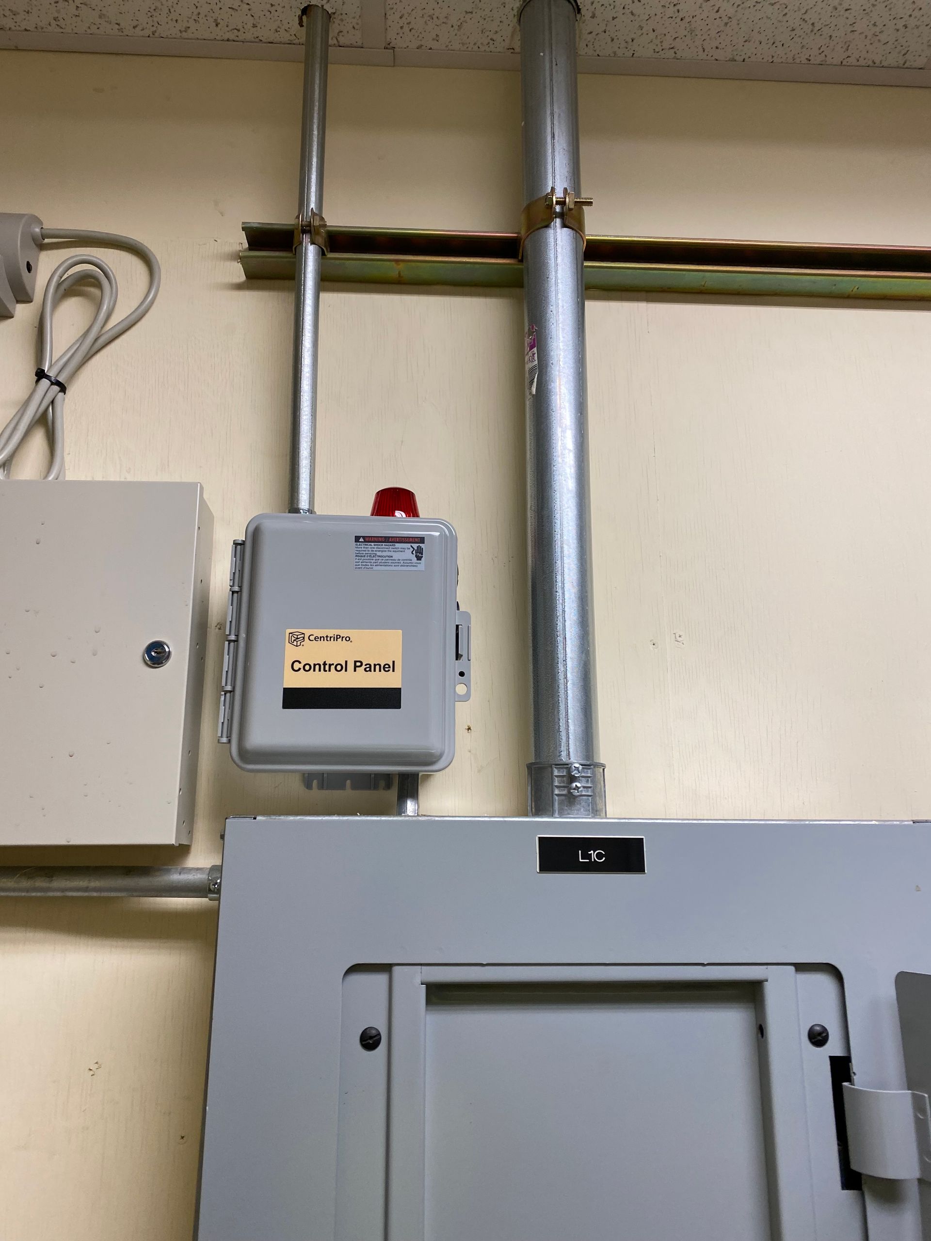 Gray electrical panels and conduit pipes mounted on a beige wall in an industrial interior.