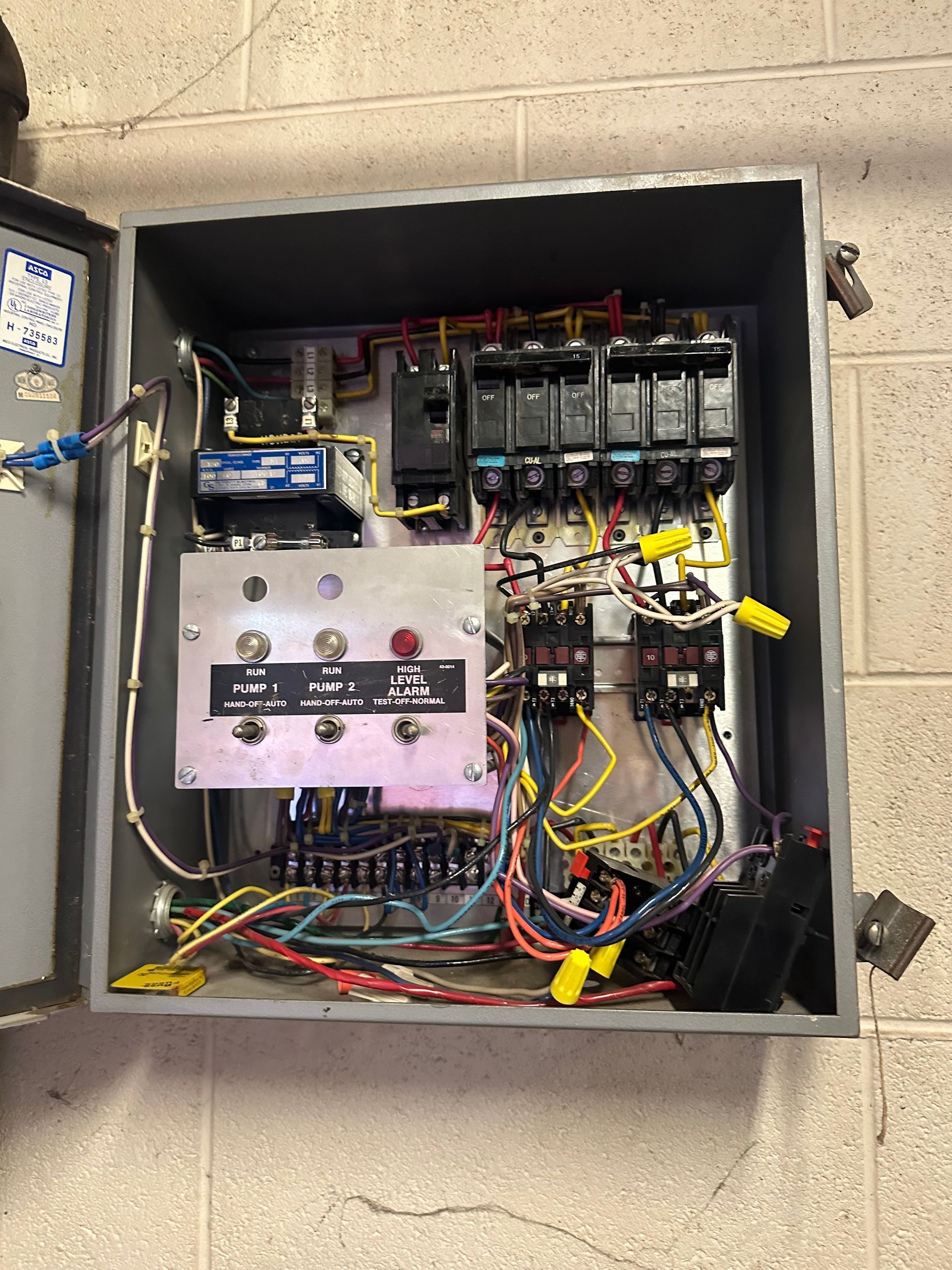 Open electrical control panel with wiring, relays, and switches in a wall-mounted metal box
