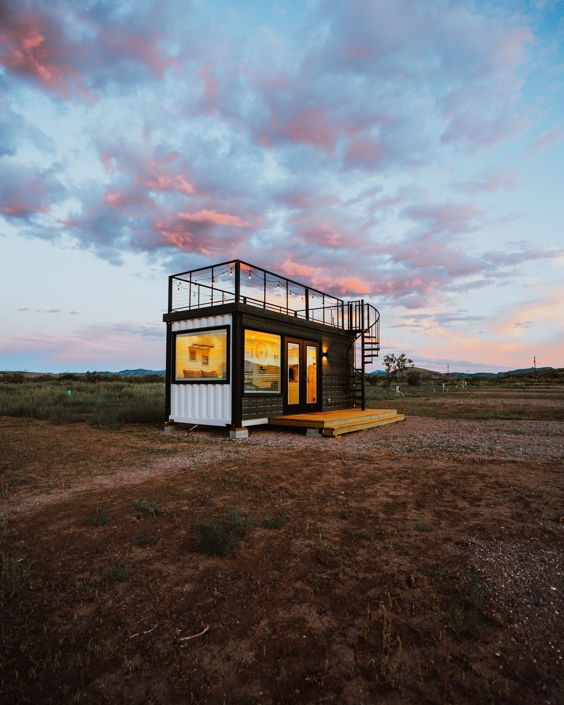 A small house is sitting in the middle of a dirt field.
