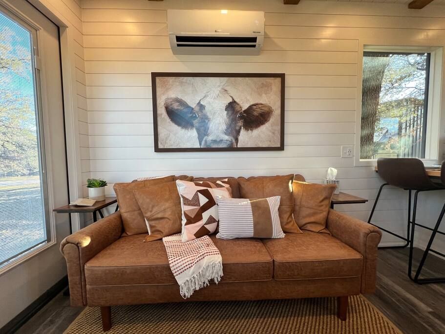 A living room with a brown couch and a picture of a cow on the wall.