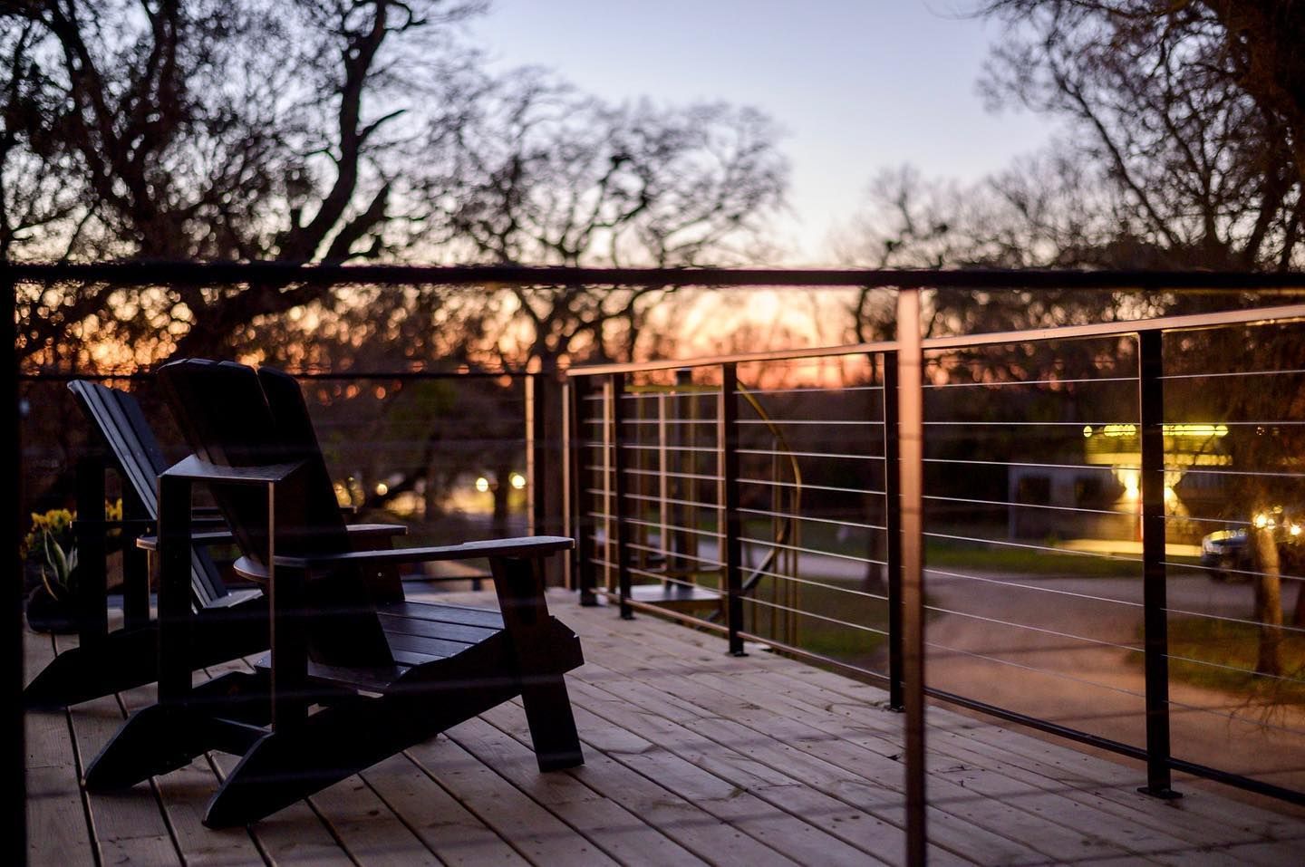 Two chairs are sitting on a deck with a sunset in the background.