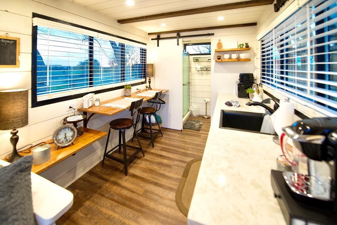 A kitchen with a sink, stools, a desk and a window.