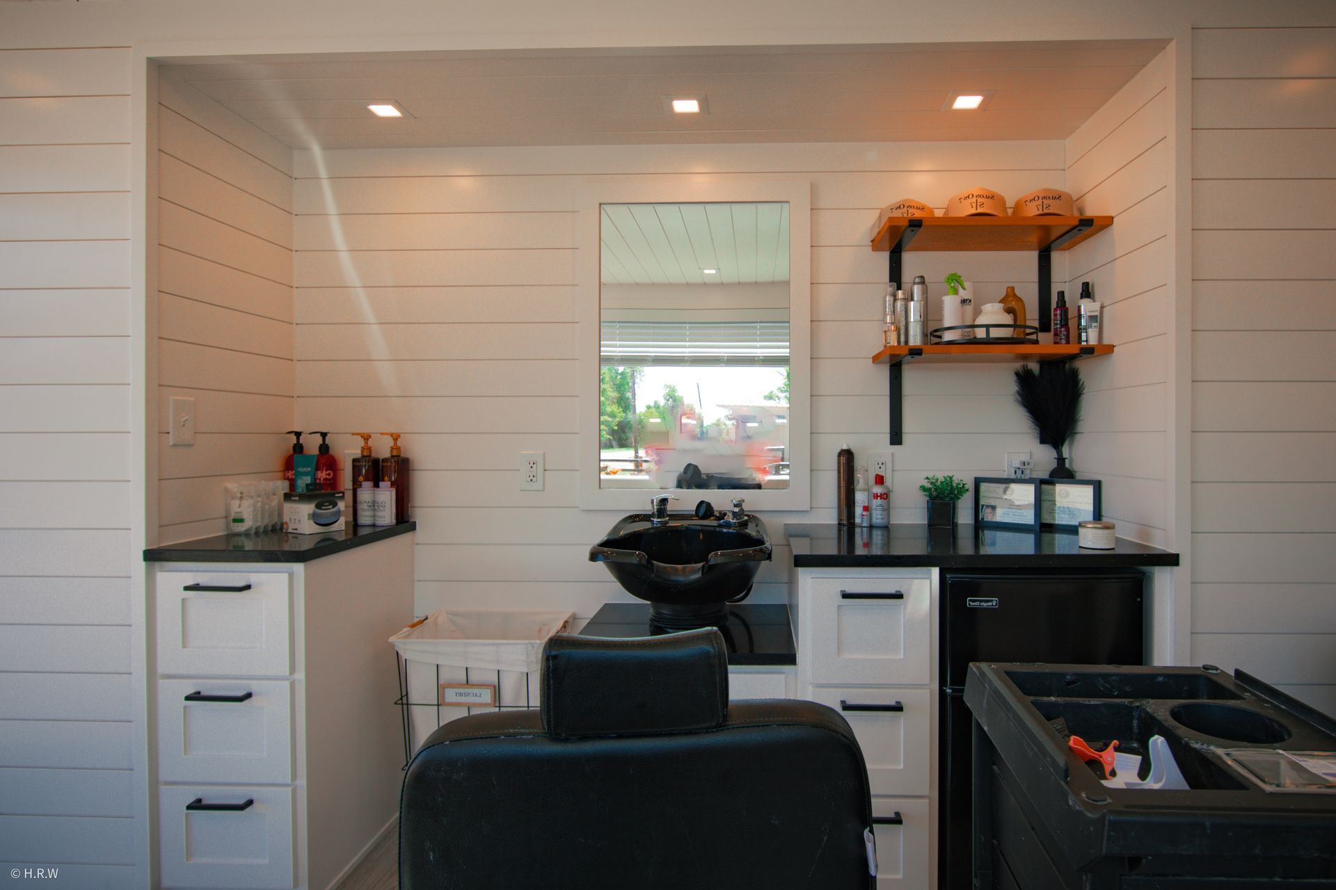a hair salon with a chair, sink, mirror and shelves