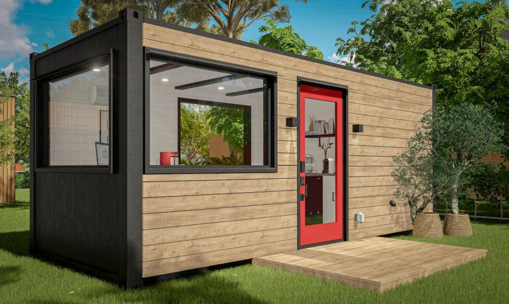 A small house with a red door and a large window is sitting on top of a lush green field.