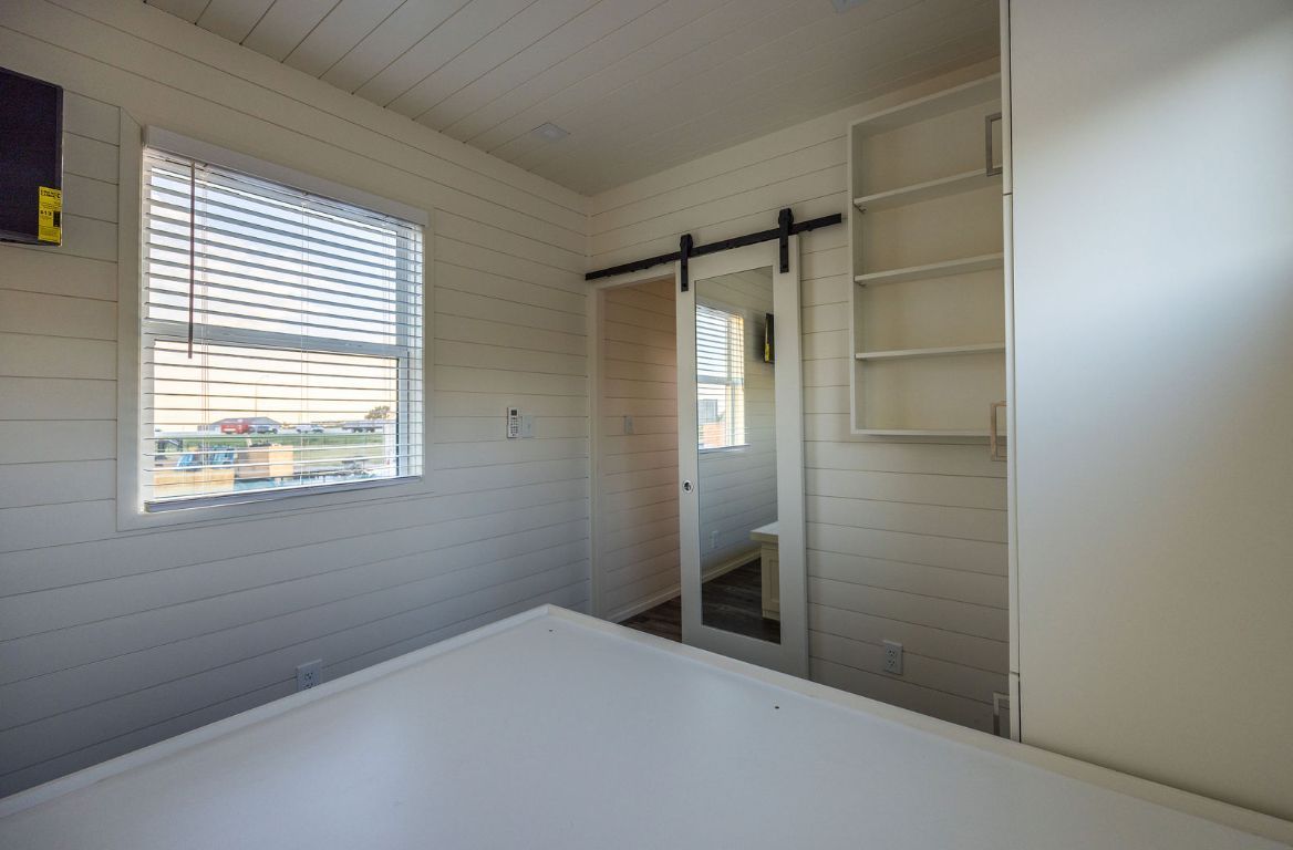 Bedroom with white walls, window with blinds, sliding door with mirror, and built-in shelving.