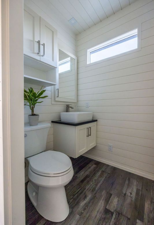 White bathroom with toilet, floating vanity, wood-look floor, and a small window.