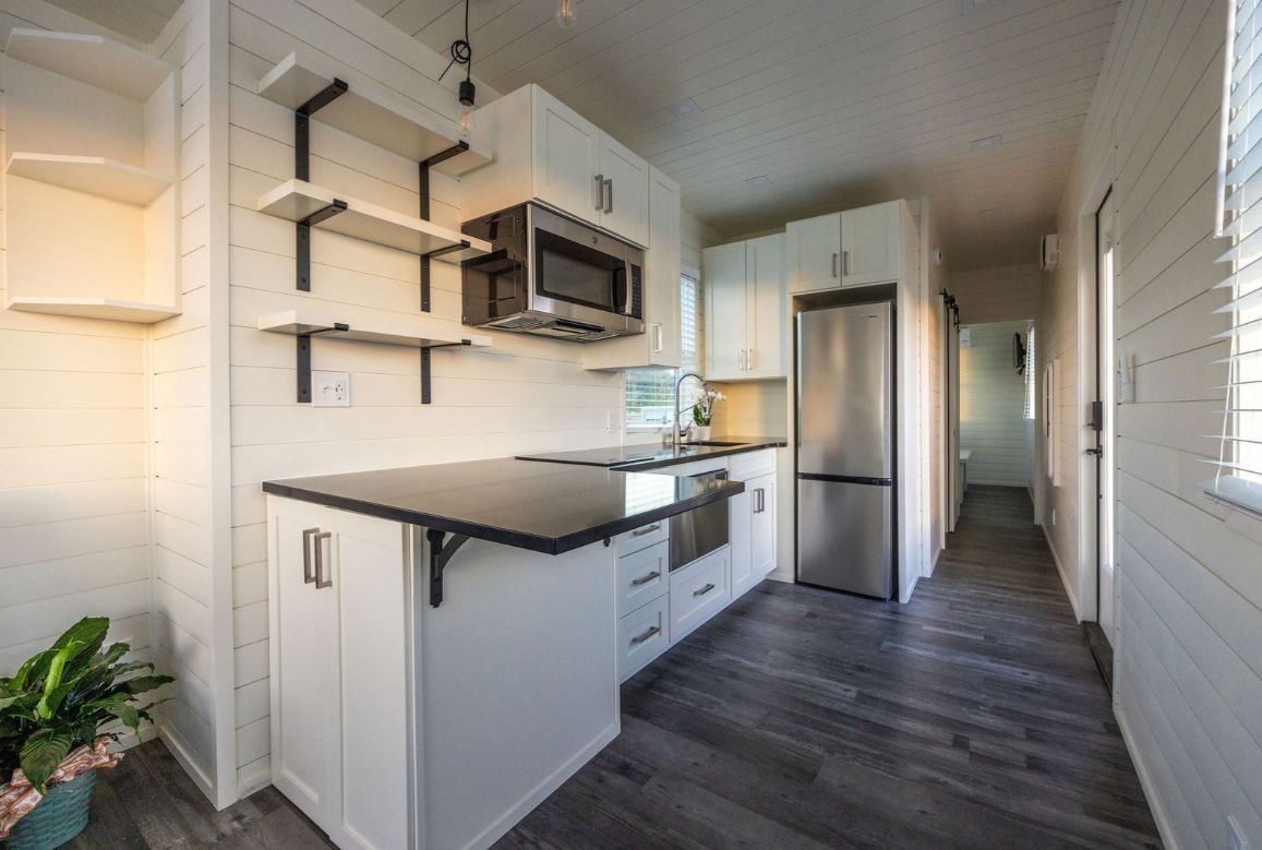 Modern tiny kitchen with white cabinets, stainless steel appliances, and dark countertops.