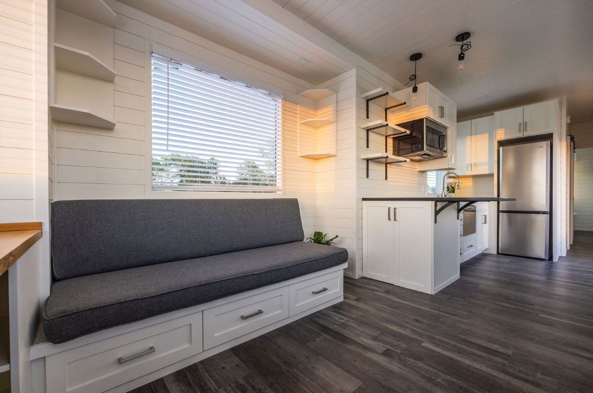 Interior of a tiny house with a built-in bench seat, kitchen, and stainless steel refrigerator.
