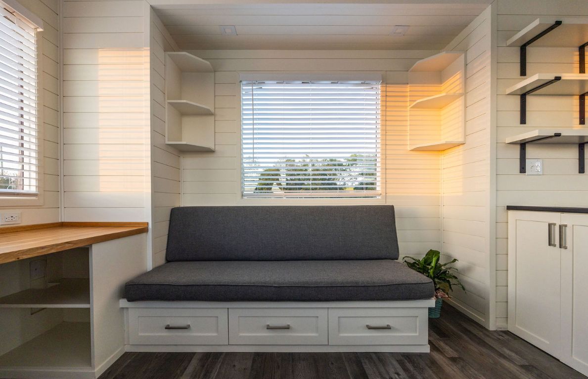 Cozy built-in seating area in tiny home with shelves, window, and storage drawers.