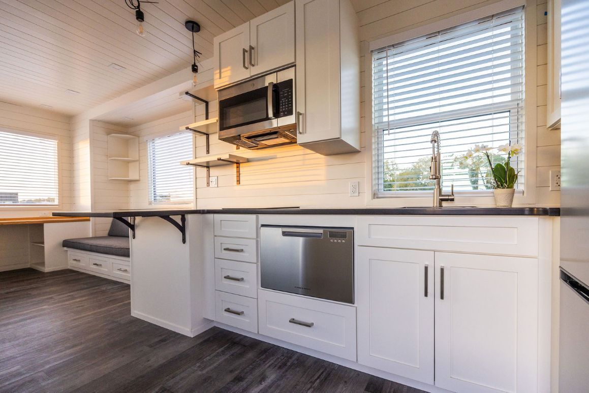 White kitchen with cabinets, stainless steel appliances, dark countertops, and a built-in bench seat.