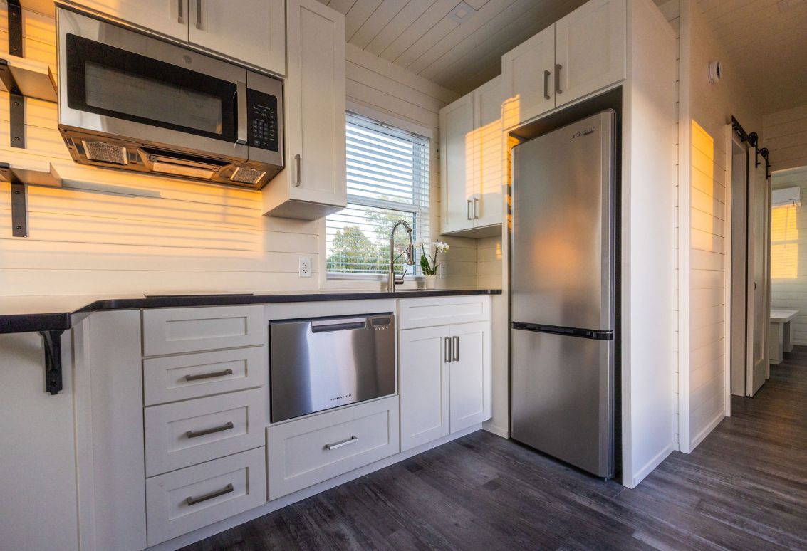 Modern kitchen in a tiny home with white cabinets, stainless steel appliances, and dark countertops.