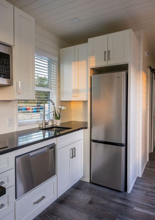Small kitchen with white cabinets, stainless steel appliances, dark countertop, and window with blinds.