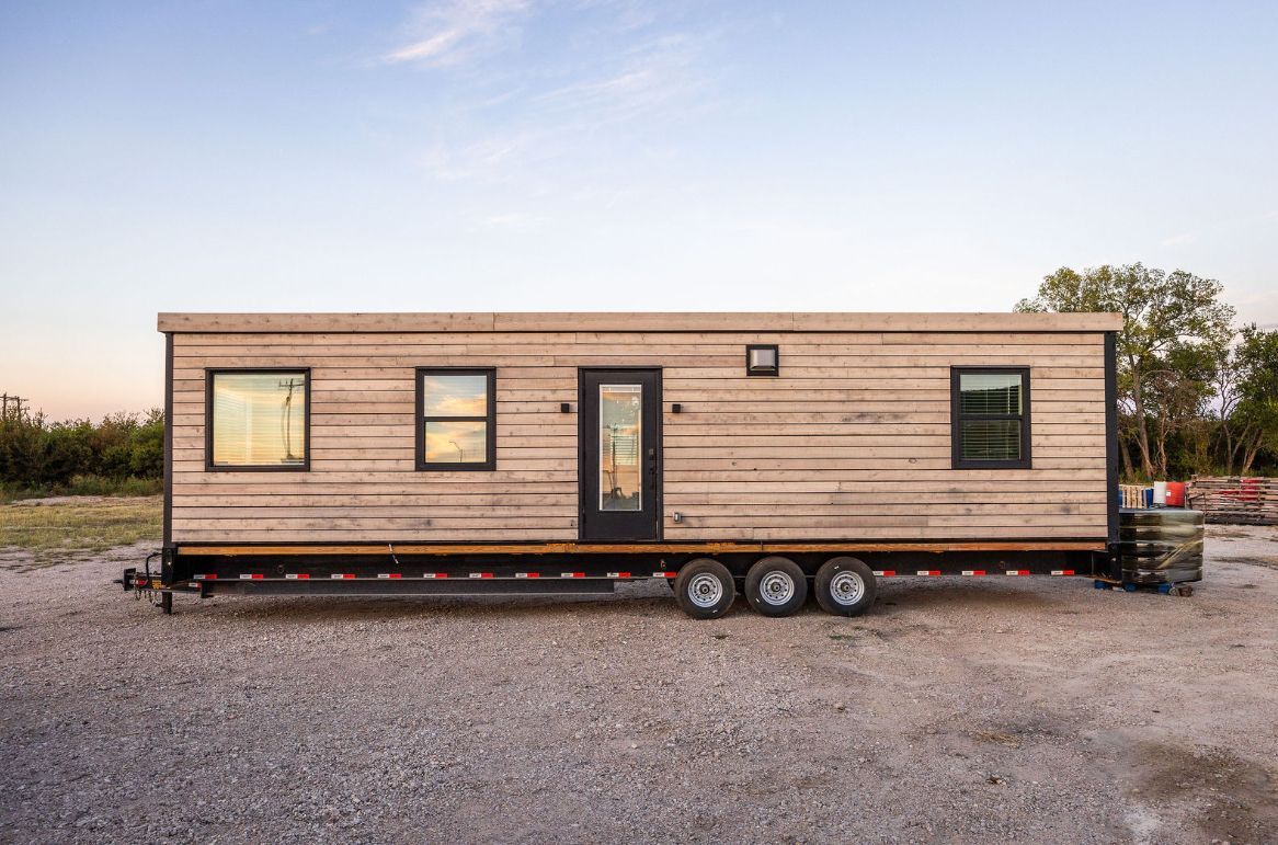 A tiny house on a trailer with wood siding and black-framed windows.
