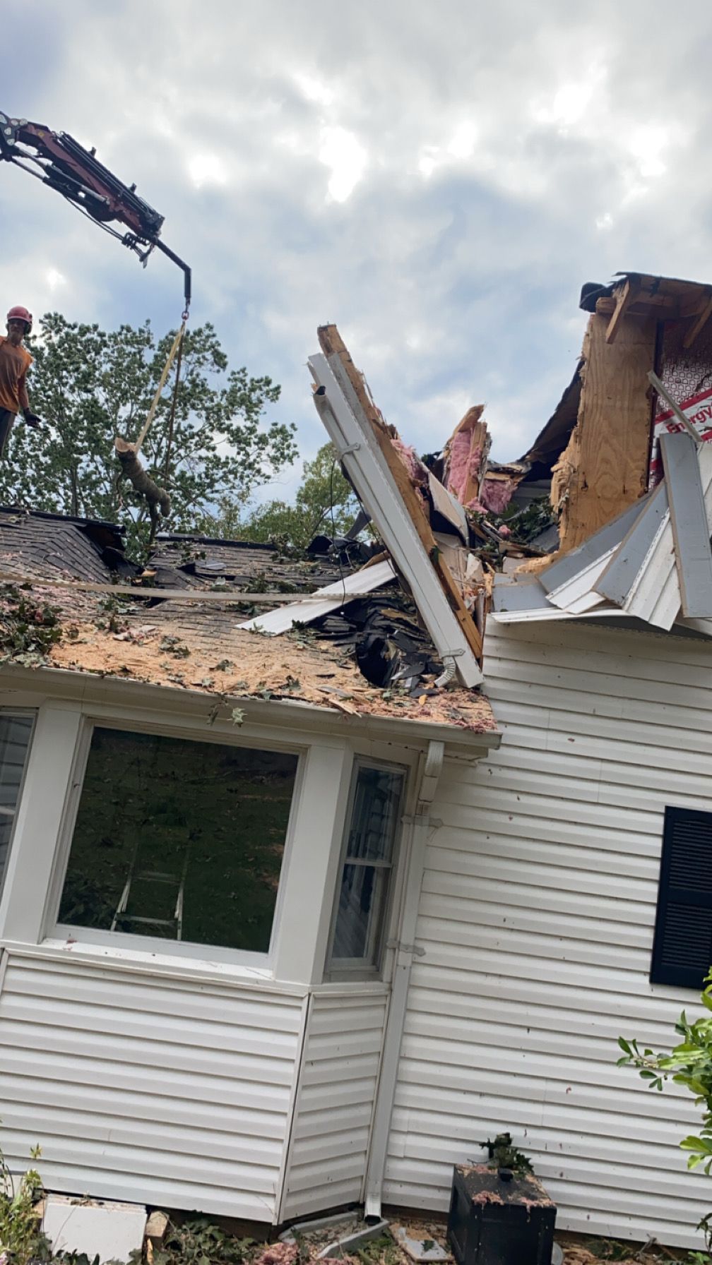 A white house with a broken roof is being demolished by a crane.