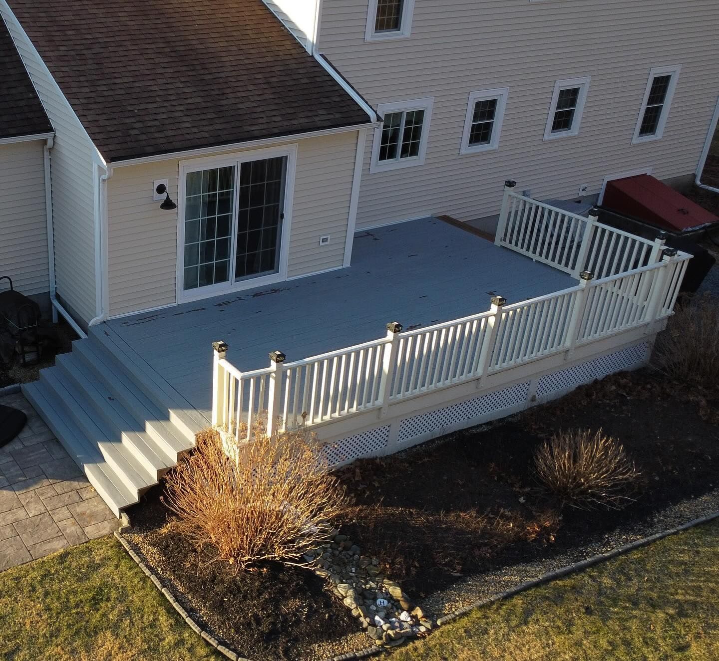 An elevated view of a gray deck with white railings, stairs, and a sliding glass door attached to a beige house.