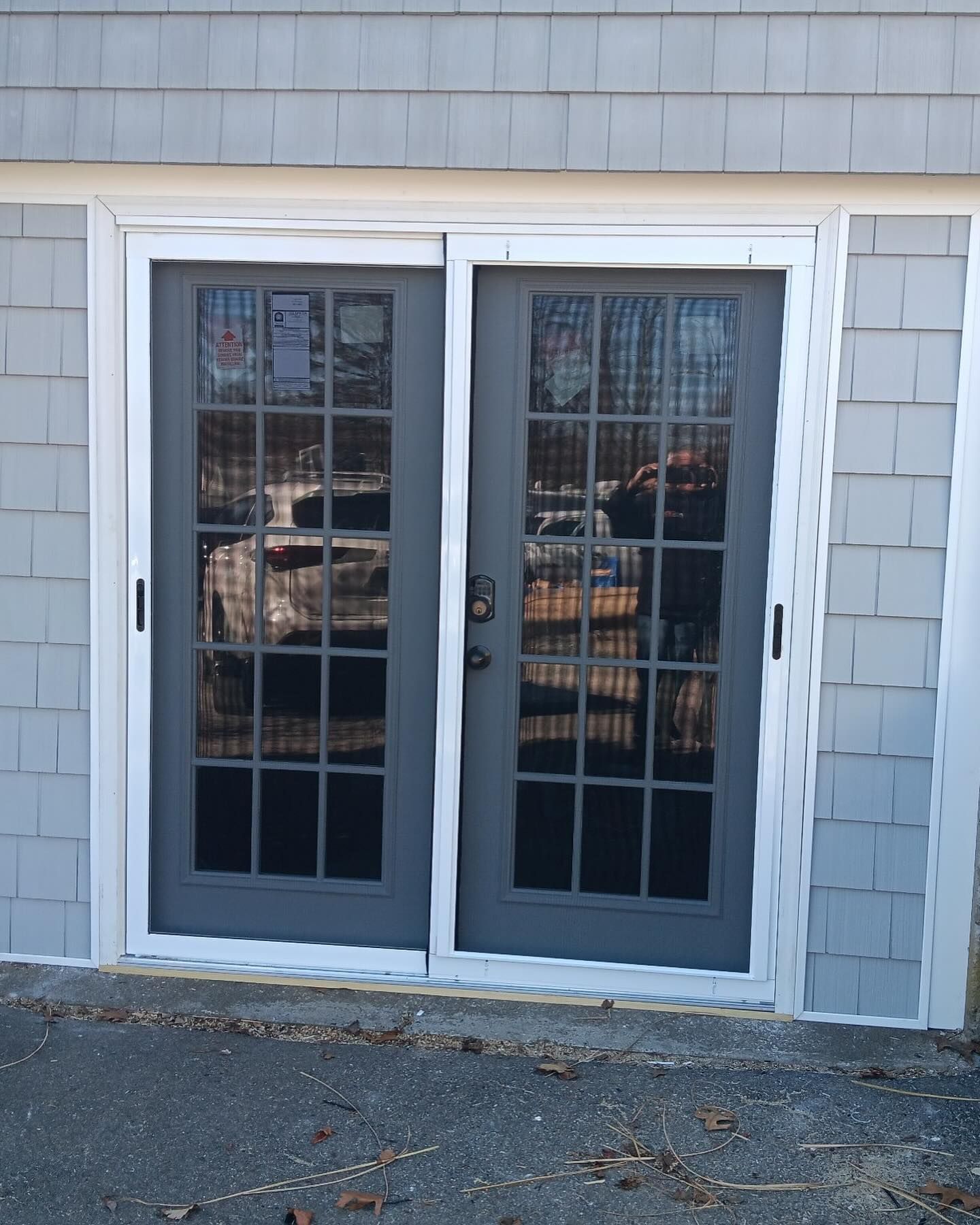 A pair of gray-framed French doors with multiple glass panes, installed in a home with gray shingle siding.