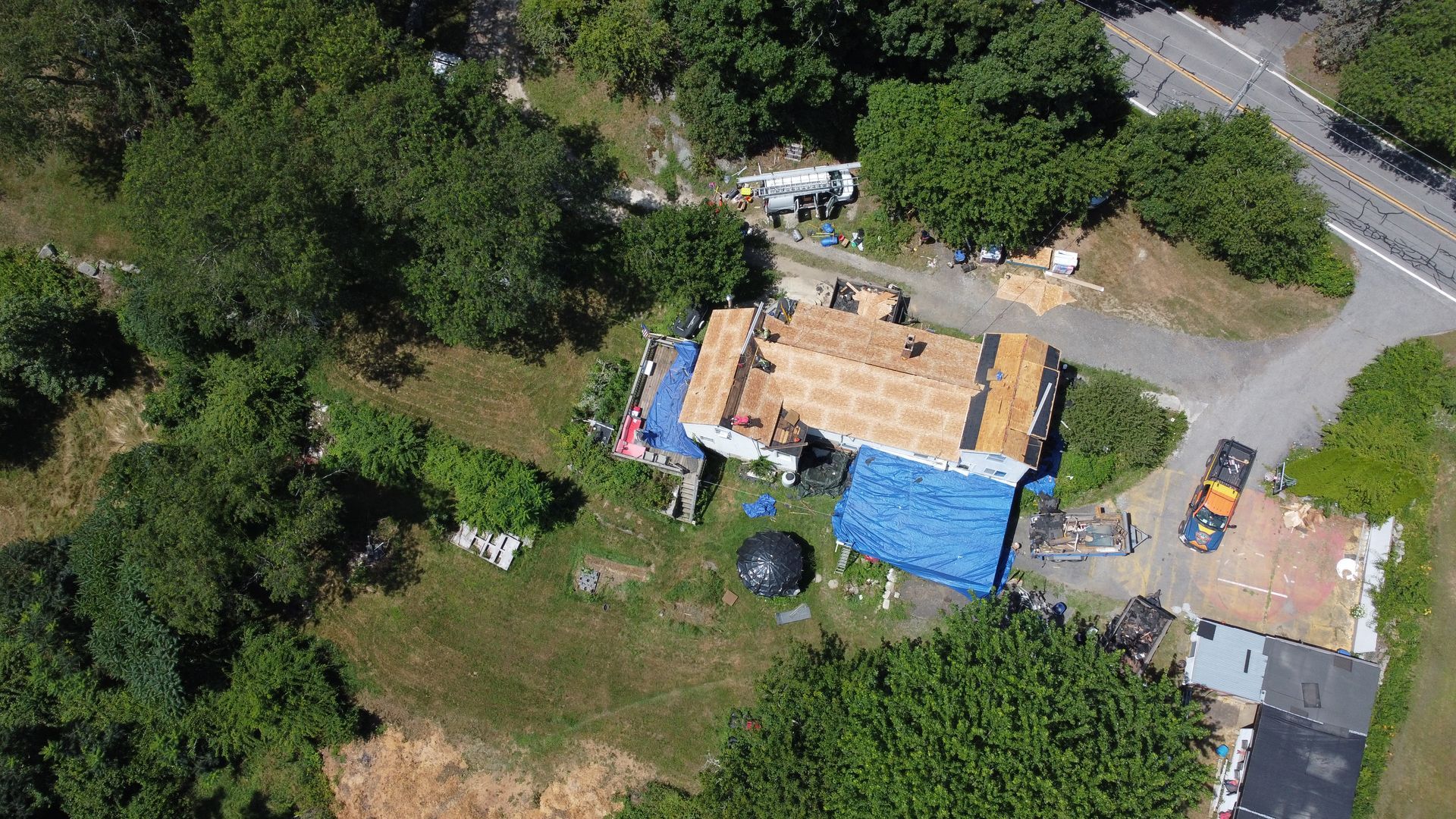 Aerial view of a house with blue tarps, surrounded by trees and a winding driveway