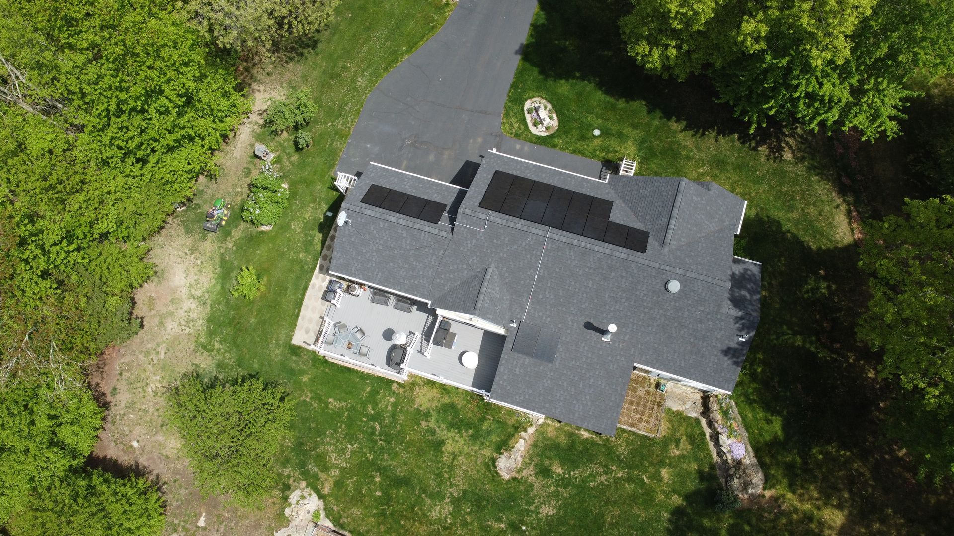 Aerial view of a gray-roofed house surrounded by trees and grass, with a driveway on the left.