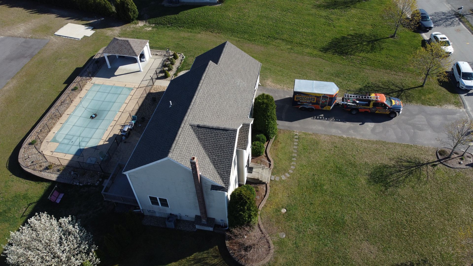 Aerial view of a house with a rectangular swimming pool and a pickup truck with equipment in the driveway.