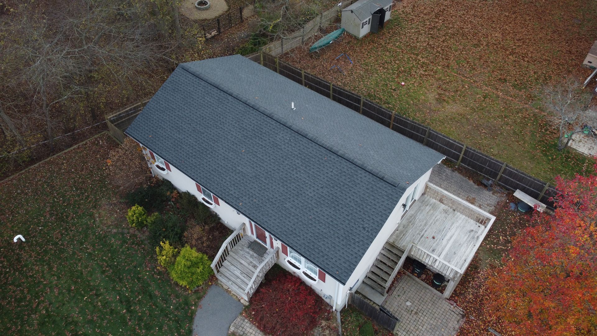 Aerial view of a gray-roofed house with white siding, surrounded by trees and a small deck.