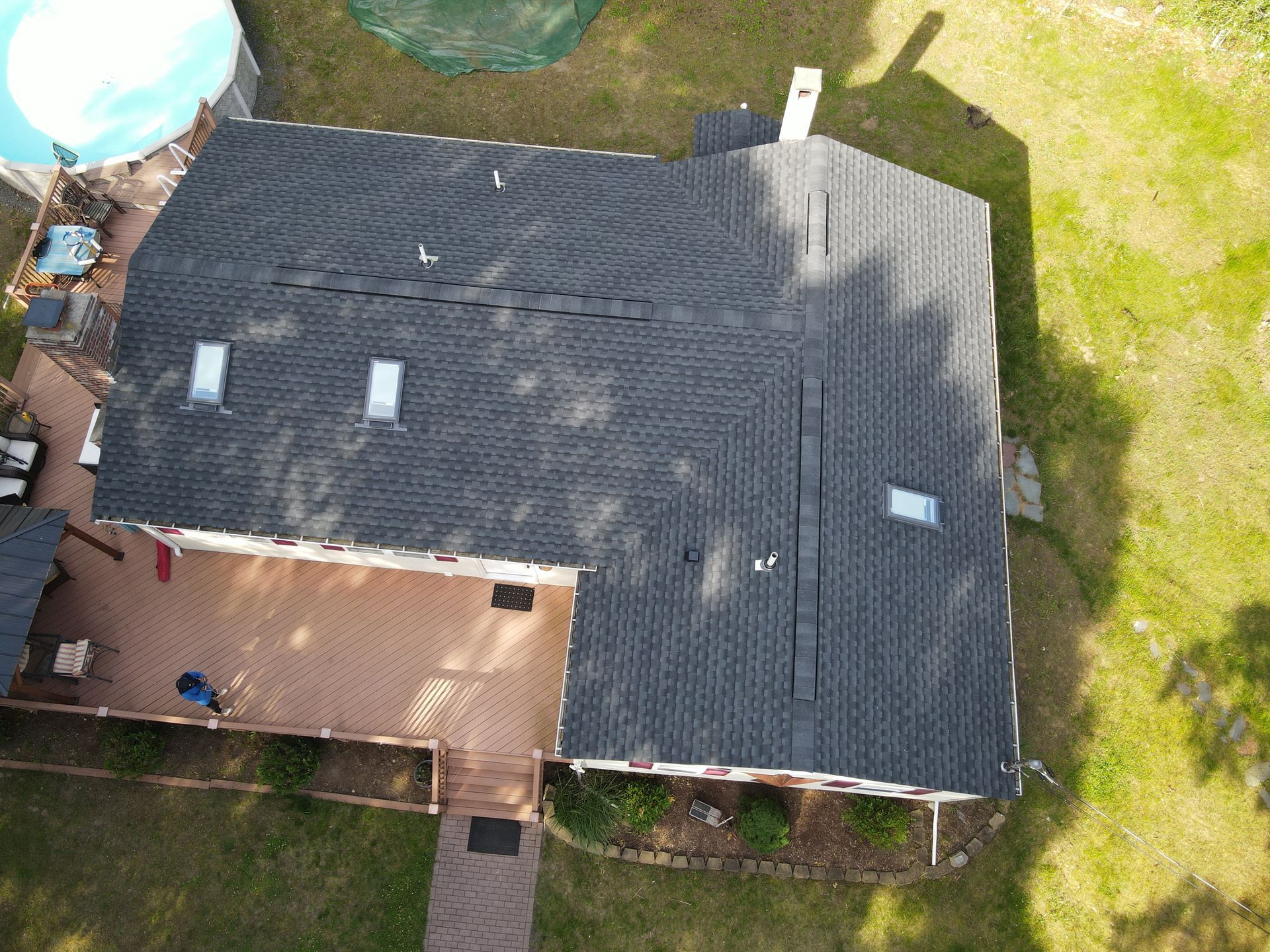 Aerial view of a dark gray roof with skylights, attached to a wooden deck and surrounded by green lawn.