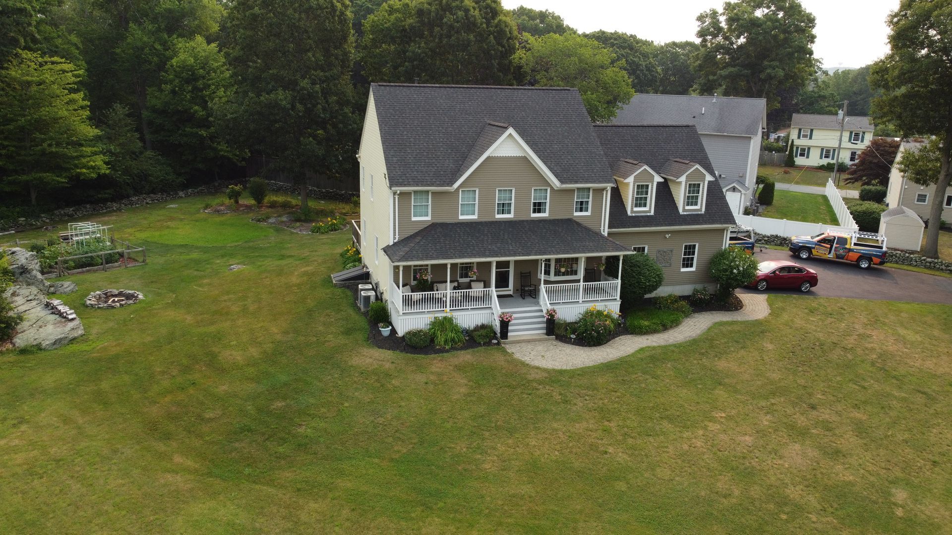 A gray two-story house with a large front porch, surrounded by a grassy yard and trees.