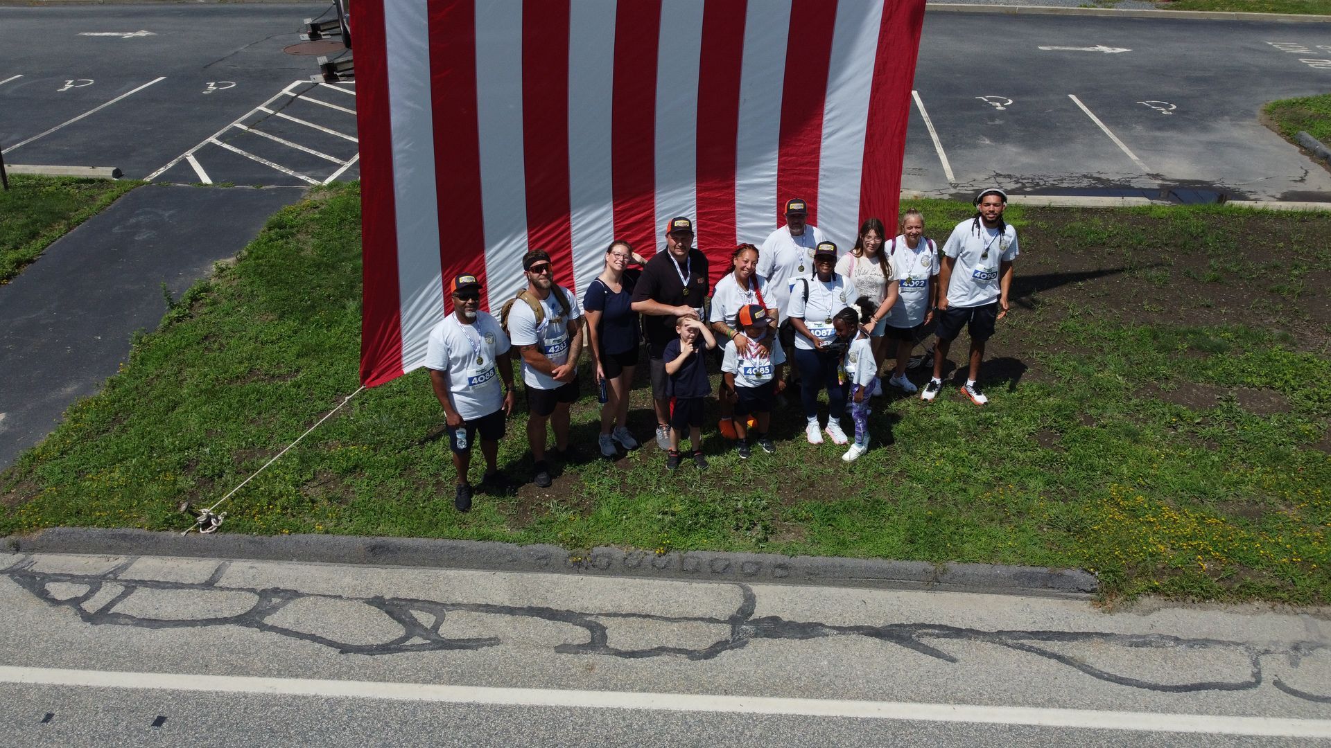 Group of people standing by a large red-and-white striped flag outdoors near a parking lot