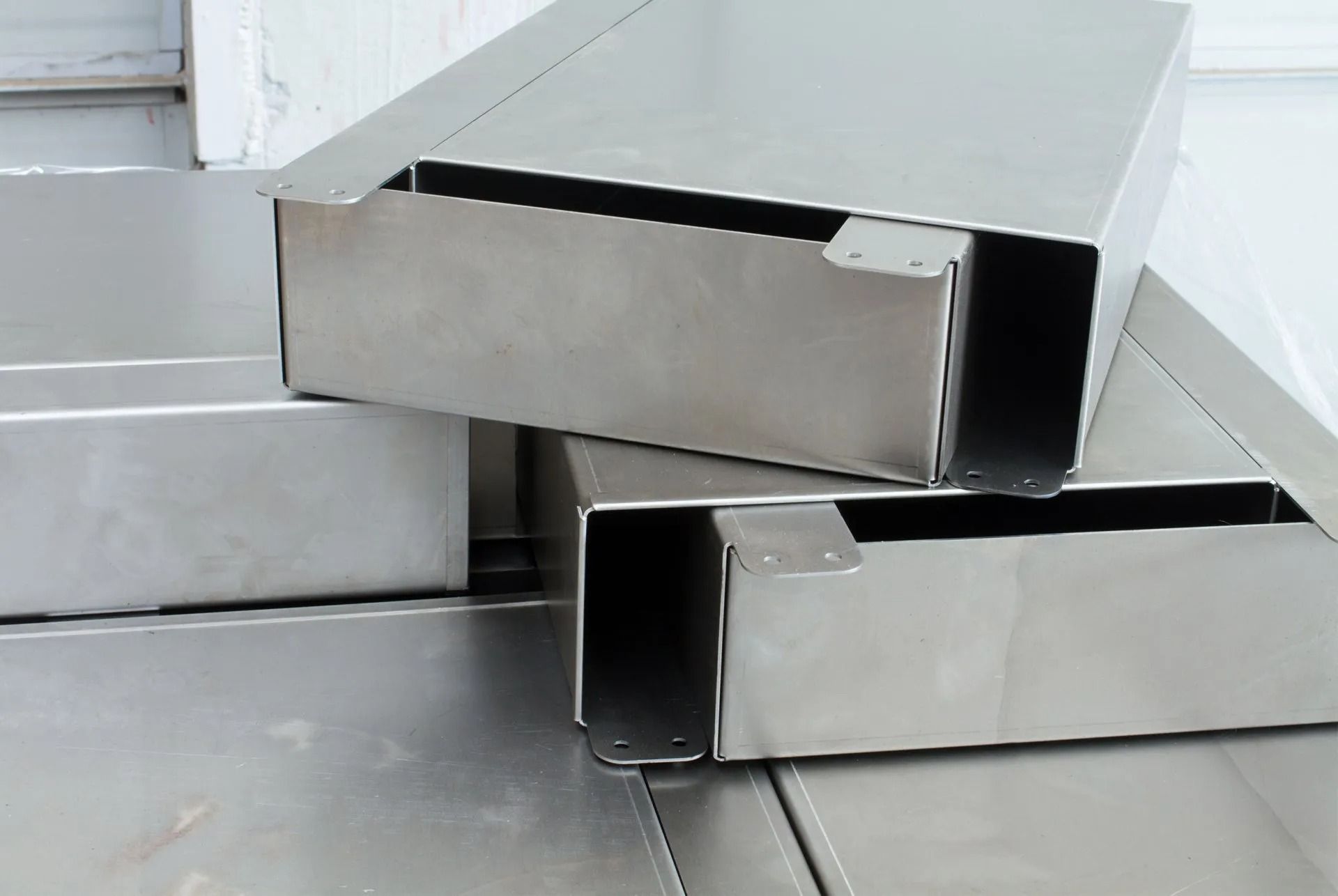 Three stacked, unpainted stainless steel rectangular metal enclosures with open ends sitting on a flat metal surface.