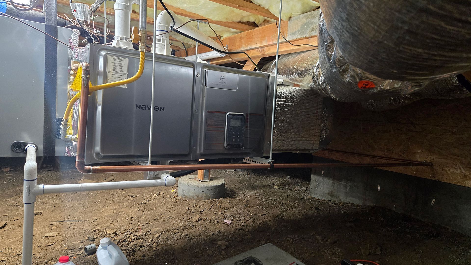 A Navien tankless water heater installed in a crawl space with attached copper and PVC plumbing.