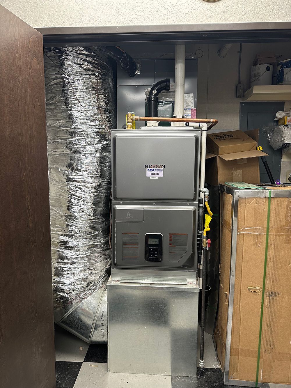 A Rheem furnace unit installed in a utility closet with connected silver ductwork and copper piping.