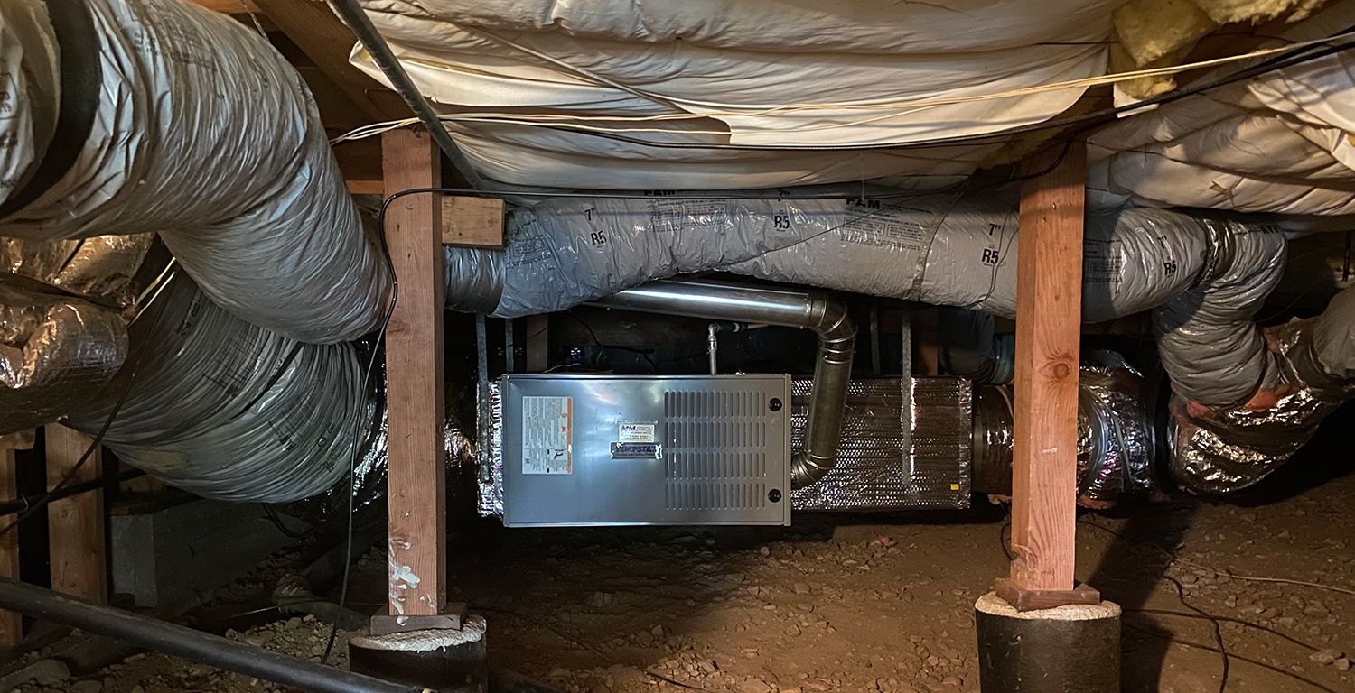 HVAC system unit suspended between wooden support posts in a crawl space with insulated ductwork.