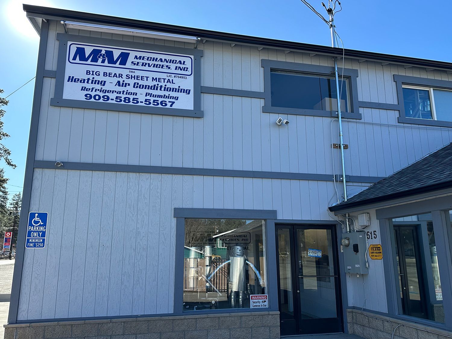 Exterior of M&M Mountain Bike Rental building with a sign showing contact info and a robot displayed in the front window.