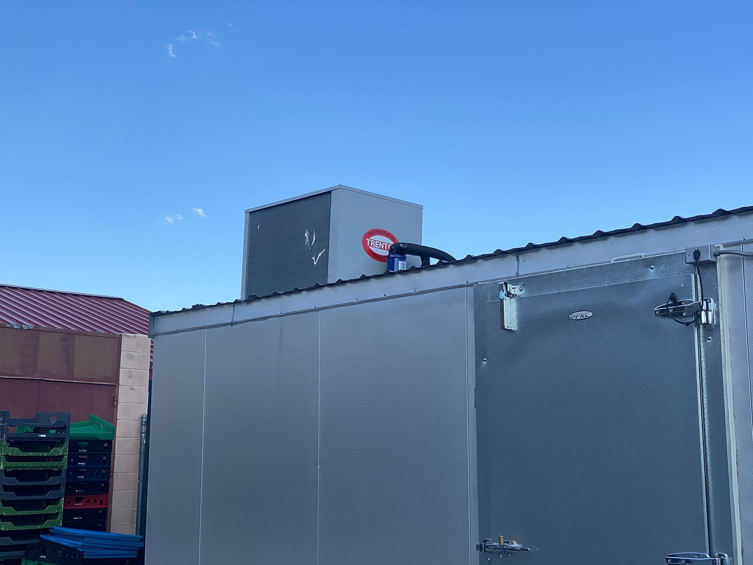 A rooftop refrigeration unit on a metal outdoor cooler, set against a clear blue sky.