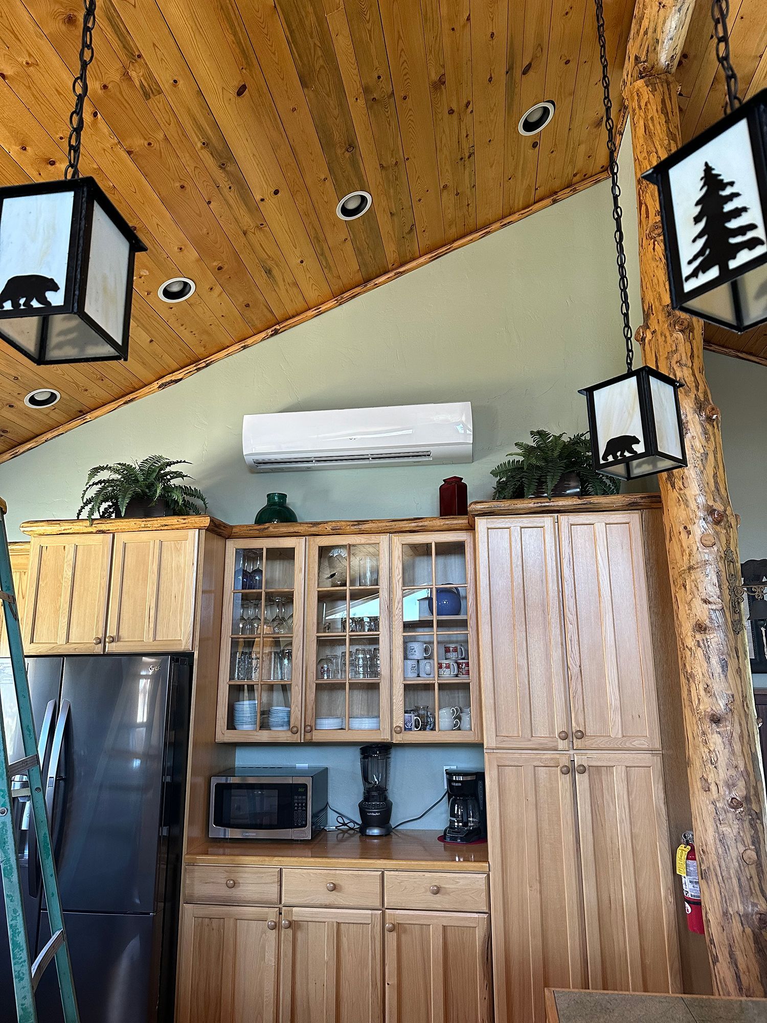 Rustic kitchen with wooden cabinets, hanging lantern-style lights, and a wall-mounted mini-split HVAC unit above.