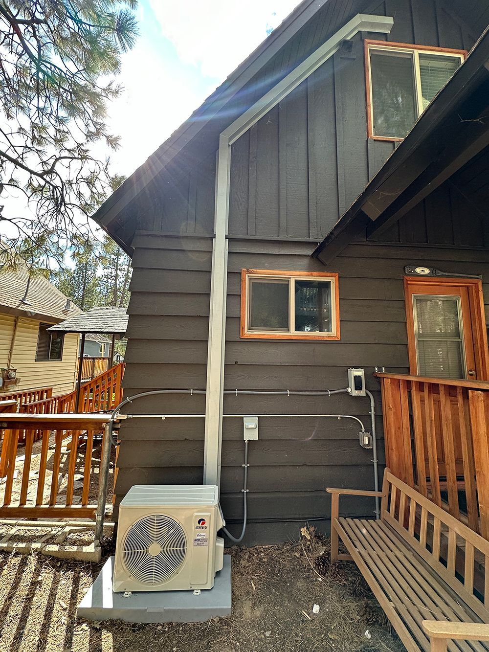 An outdoor HVAC unit sitting on a concrete pad next to a brown wooden cabin with a wooden bench on the right.