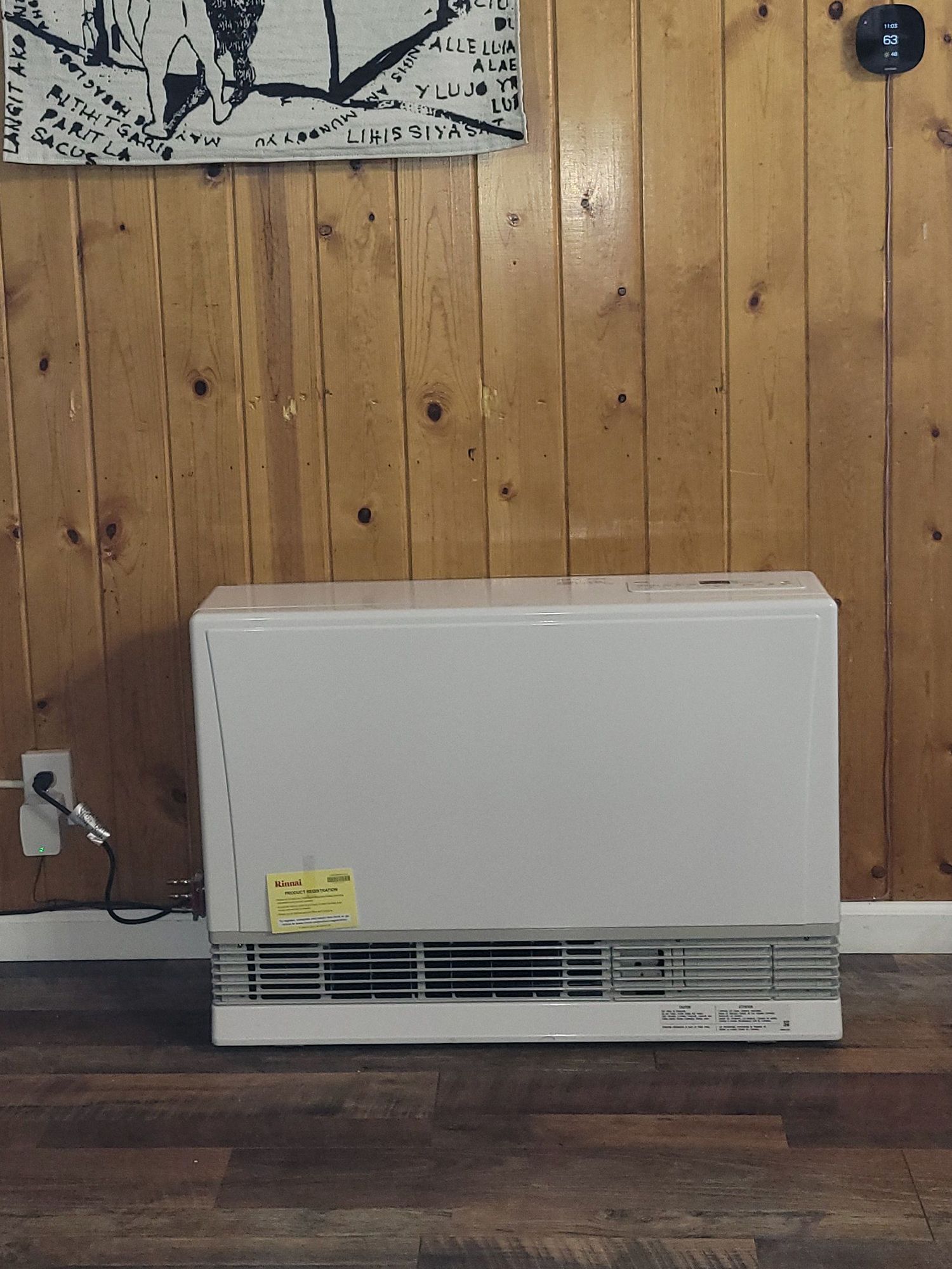 A white Rinnai space heater sits on a wood-paneled wall above a dark wood-look floor.