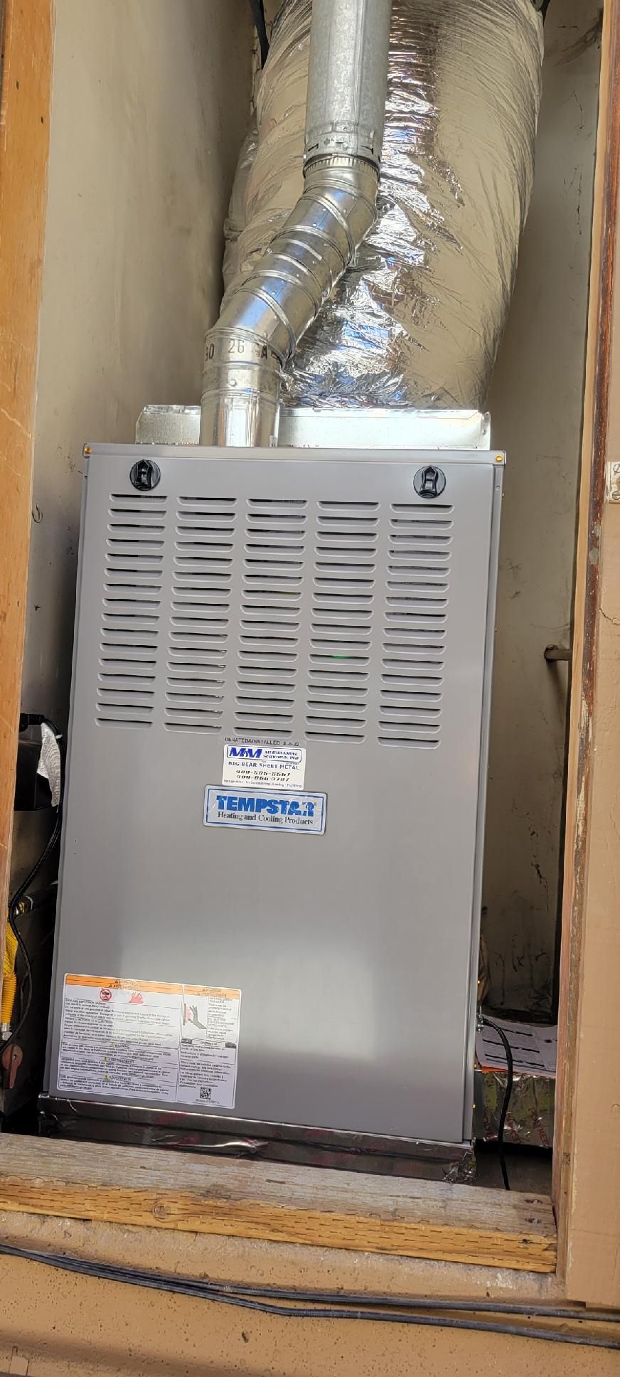 A gray residential gas furnace unit installed inside a wooden closet with an insulated exhaust vent pipe at the top.