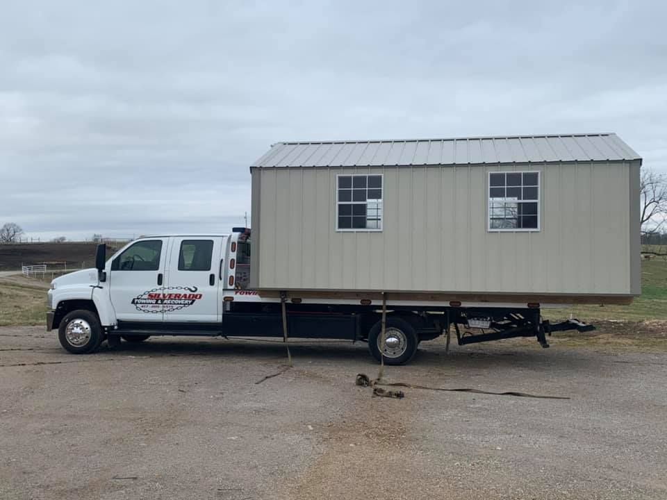 A tow truck is carrying a shed on a trailer.