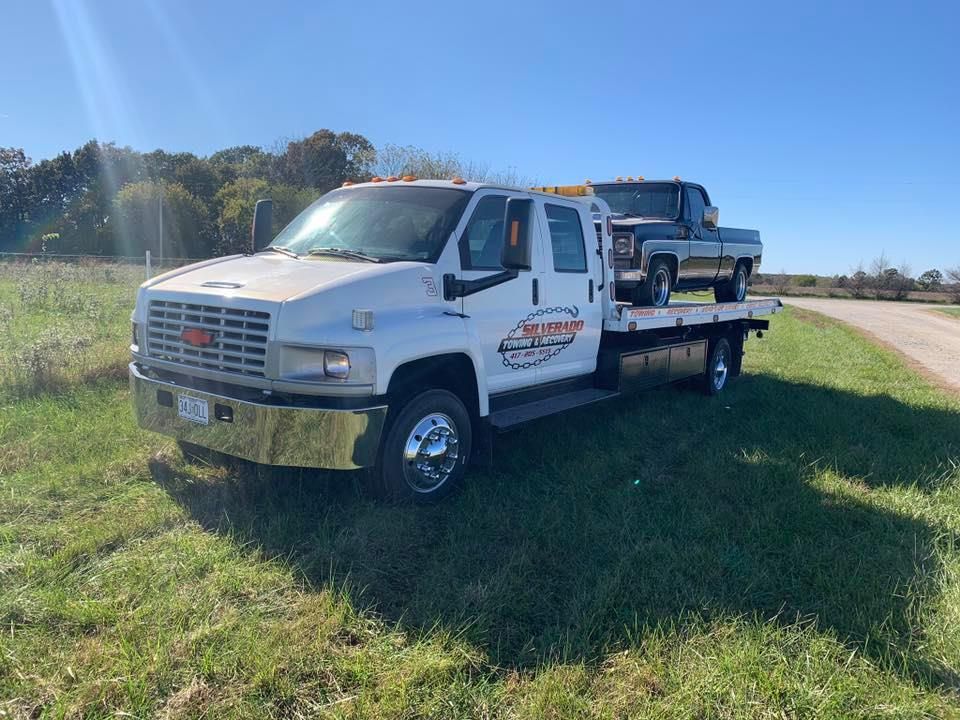 A white tow truck with two trucks on the back is parked in a grassy field.