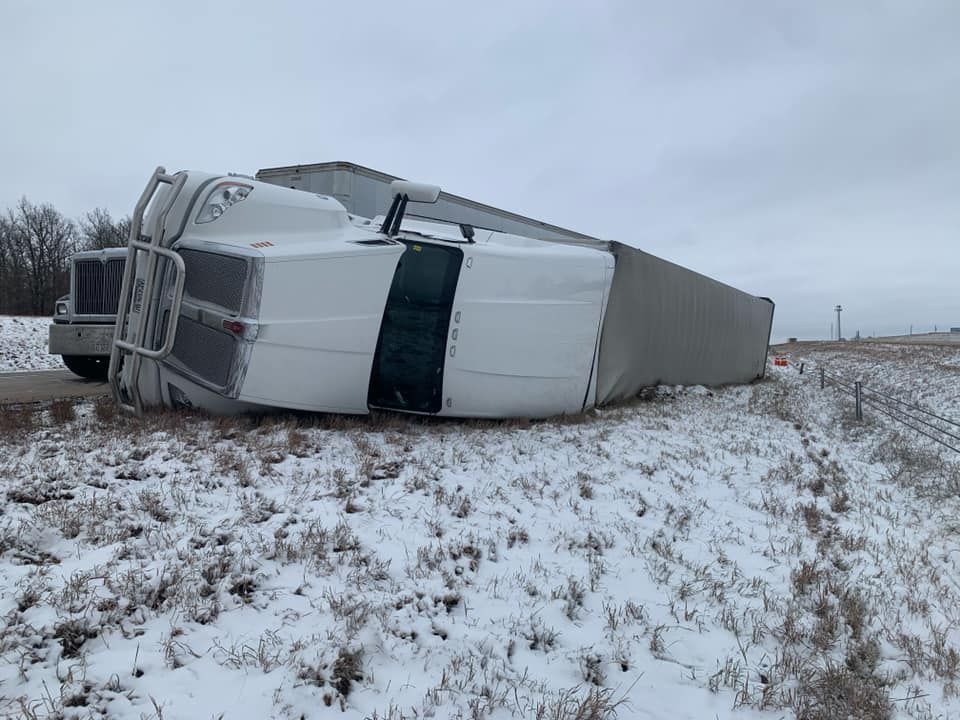 A semi truck is turned over on its side in a snowy field.
