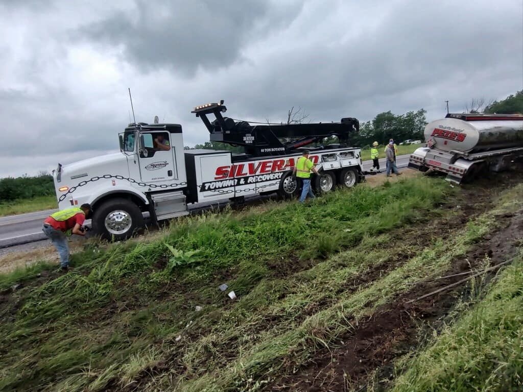 A tow truck is sitting on the side of the road next to a tanker truck.