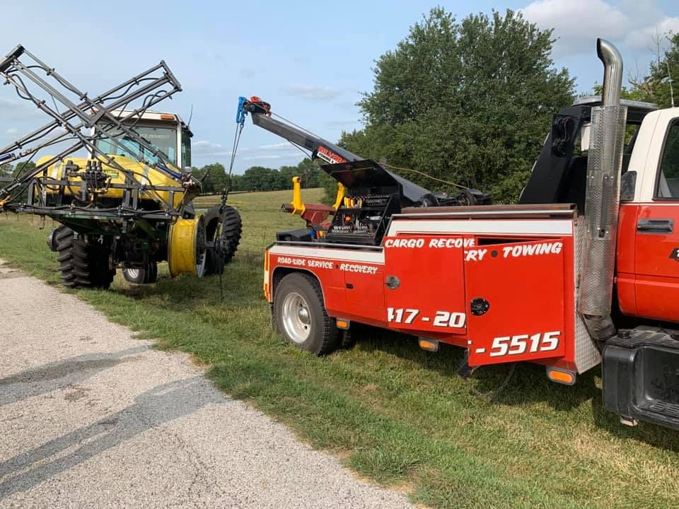 A red tow truck is towing a tractor in a field.