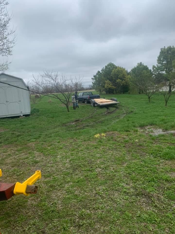 A person is holding a tool in a field with a trailer in the background.