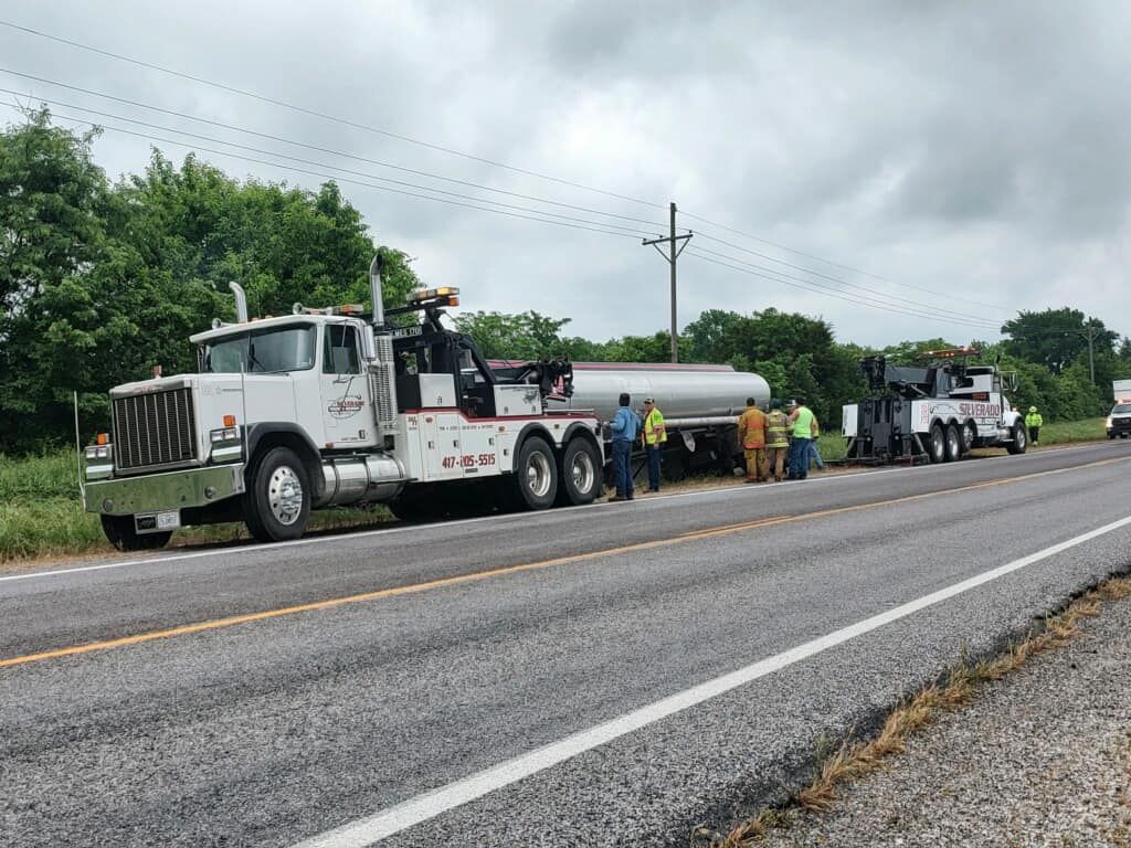 A tow truck is parked on the side of the road next to a tanker truck.