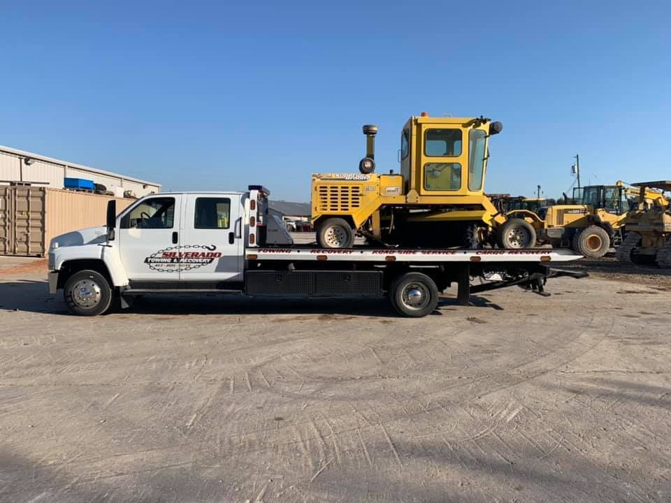 A tow truck is carrying a yellow bulldozer on the back of it.