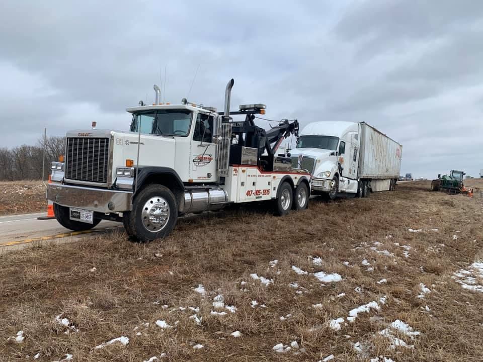 A tow truck is towing a semi truck on the side of the road.