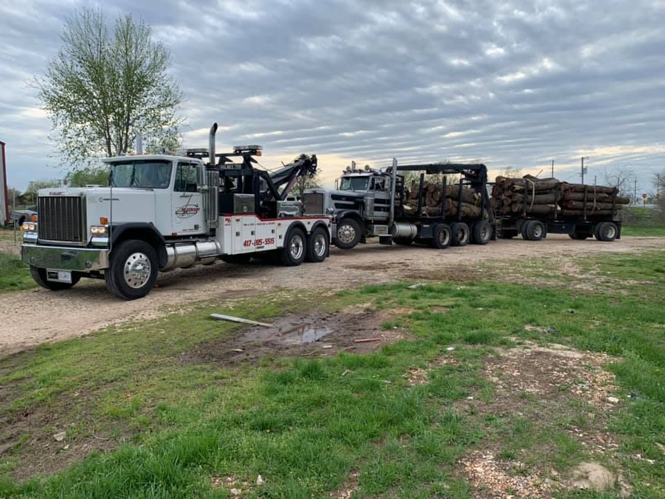 A tow truck is pulling a trailer full of logs.